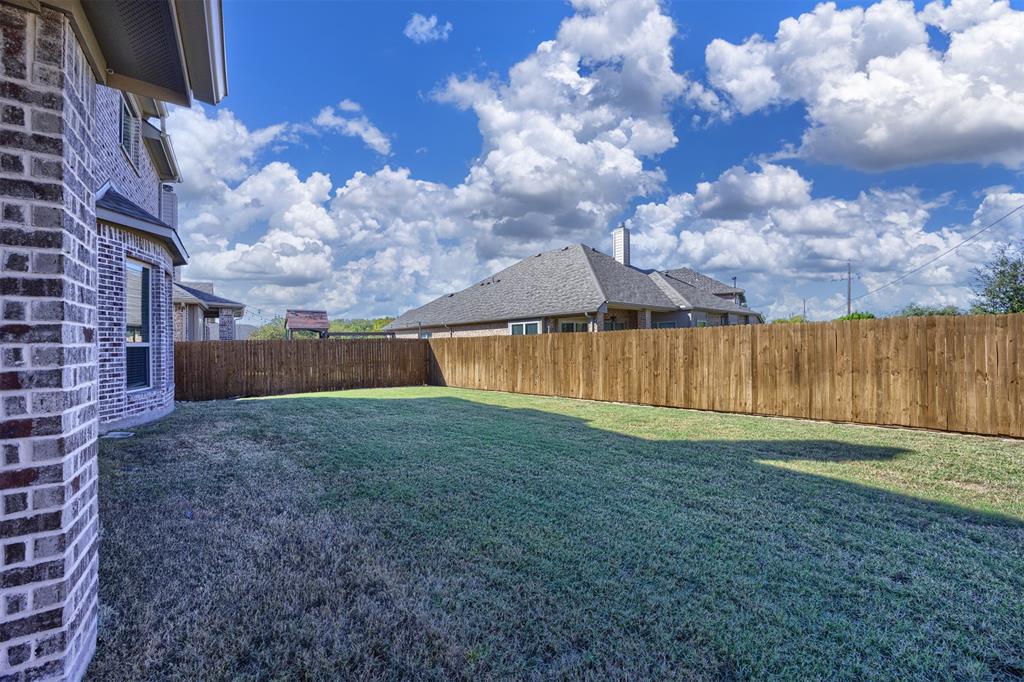 Backyard featuring a grass lawn, perimeter wood fencing, and brick exterior wall