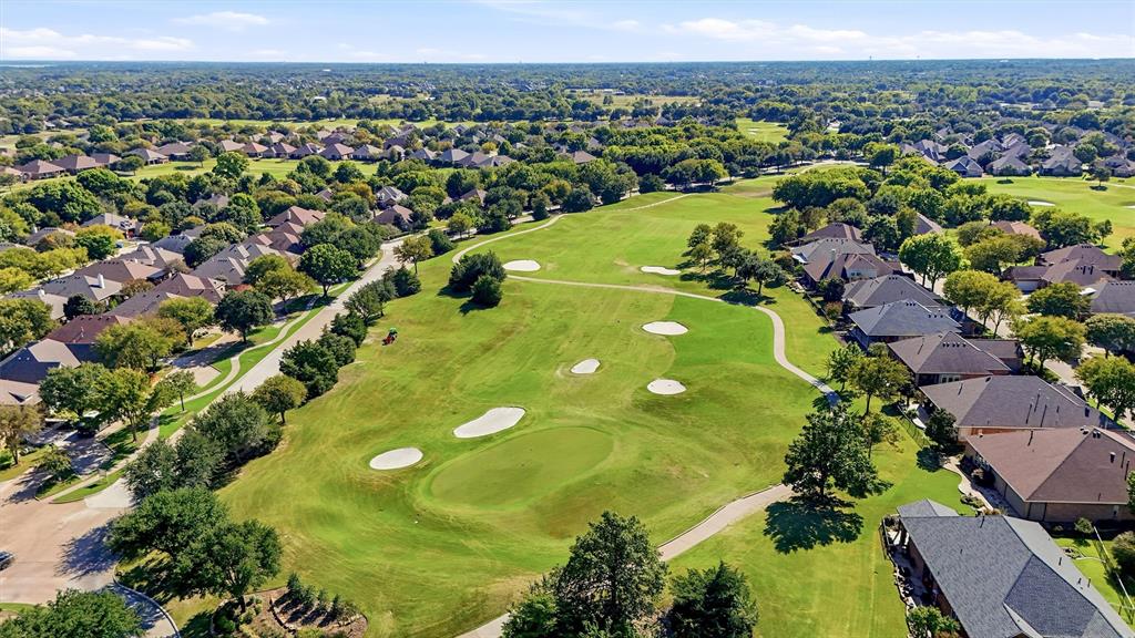 Aerial perspective of a golf course featuring manicured greens, sand bunkers, paved cart paths, and mature landscaping