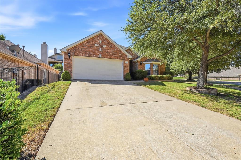Brick exterior with gable roofline, two-car garage, concrete driveway, and mature landscaping