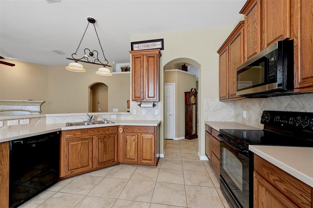 Kitchen featuring wood cabinetry, solid-surface countertops, tile backsplash, tile flooring, and integrated black appliances