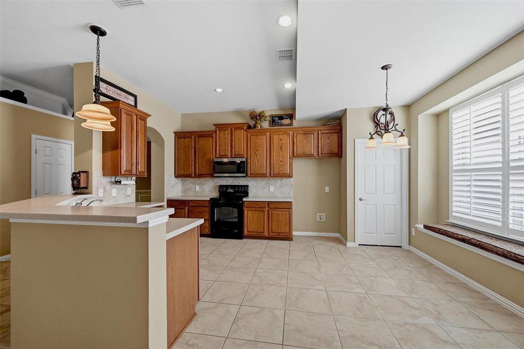Kitchen featuring stained wood cabinetry, stone-finish countertops, tile flooring, built-in black appliances, and a window seat with plantation shutters