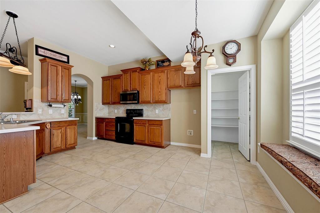 Kitchen featuring wood cabinetry, tile flooring, built-in pantry with shelving, solid surface countertops, and a window seat with plantation shutters