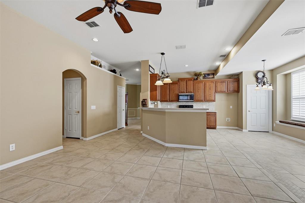 Open-concept interior featuring large-format tile flooring, wood cabinetry, built-in breakfast bar, recessed lighting, and arched doorway entry