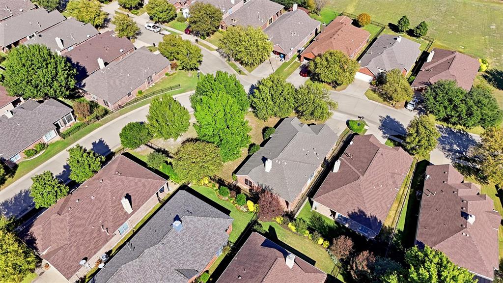 Aerial perspective of a brick residence situated on a corner lot, featuring a multi-gabled roofline, a prominent chimney, a side-entry garage, and mature landscaping