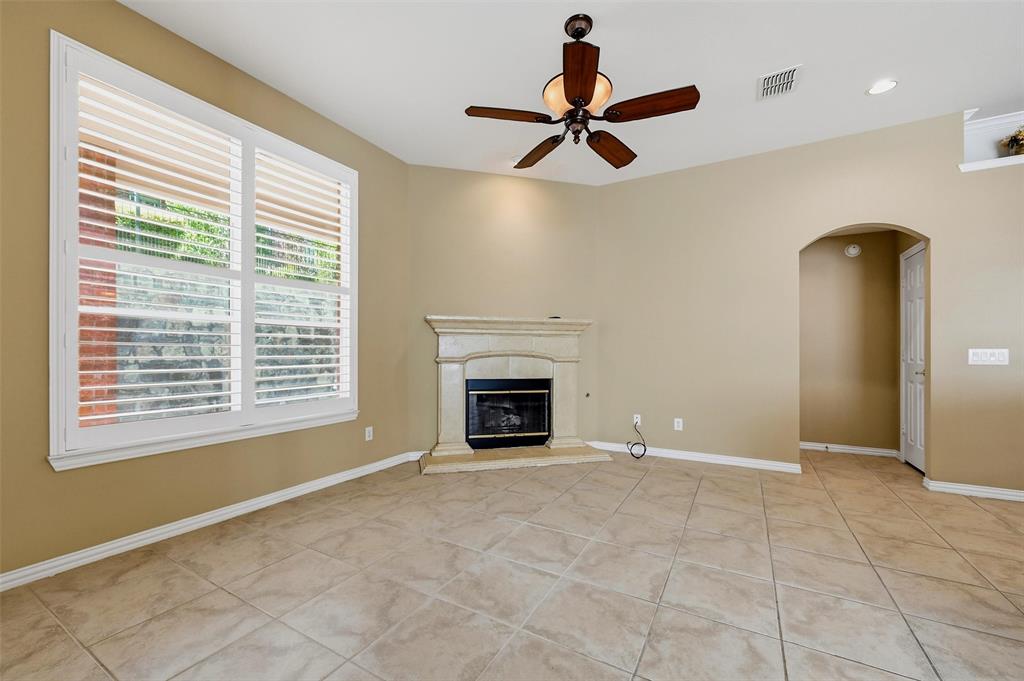 Ceramic tile flooring, stone-surround fireplace, multi-pane window with plantation shutters, ceiling fan with integrated light fixture, and arched entryway