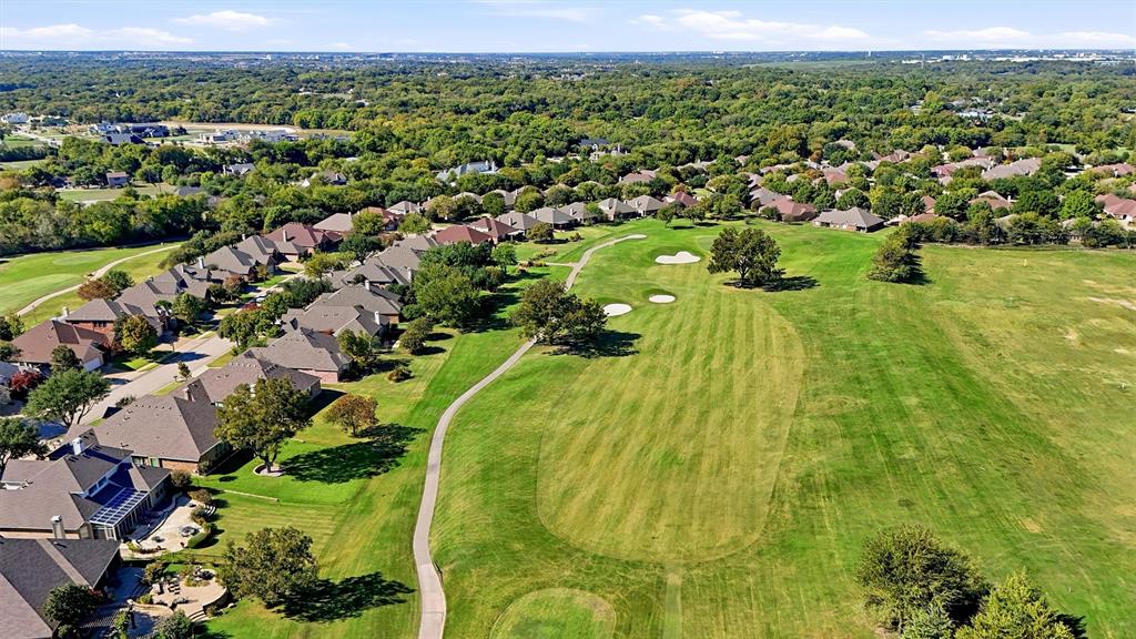 Aerial perspective of a residential community featuring expansive manicured greens, sand bunkers, mature landscaping, and concrete pathways