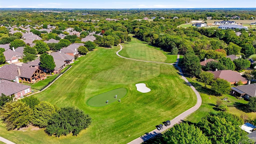 Aerial perspective of a golf course featuring manicured putting greens, sand bunkers, paved cart paths, and established tree canopy