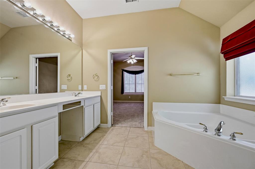 Bathroom featuring a dual-sink vanity with white cabinetry, a large wall-to-wall mirror, ceramic tile flooring, and a corner soaking tub