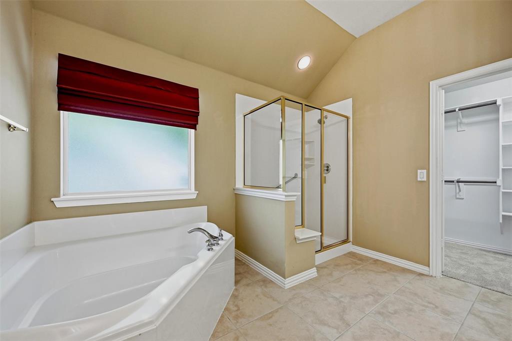 Bathroom featuring a white soaking tub, a separate glass-enclosed shower with gold-tone framing, tile flooring, and a walk-in closet with built-in shelving