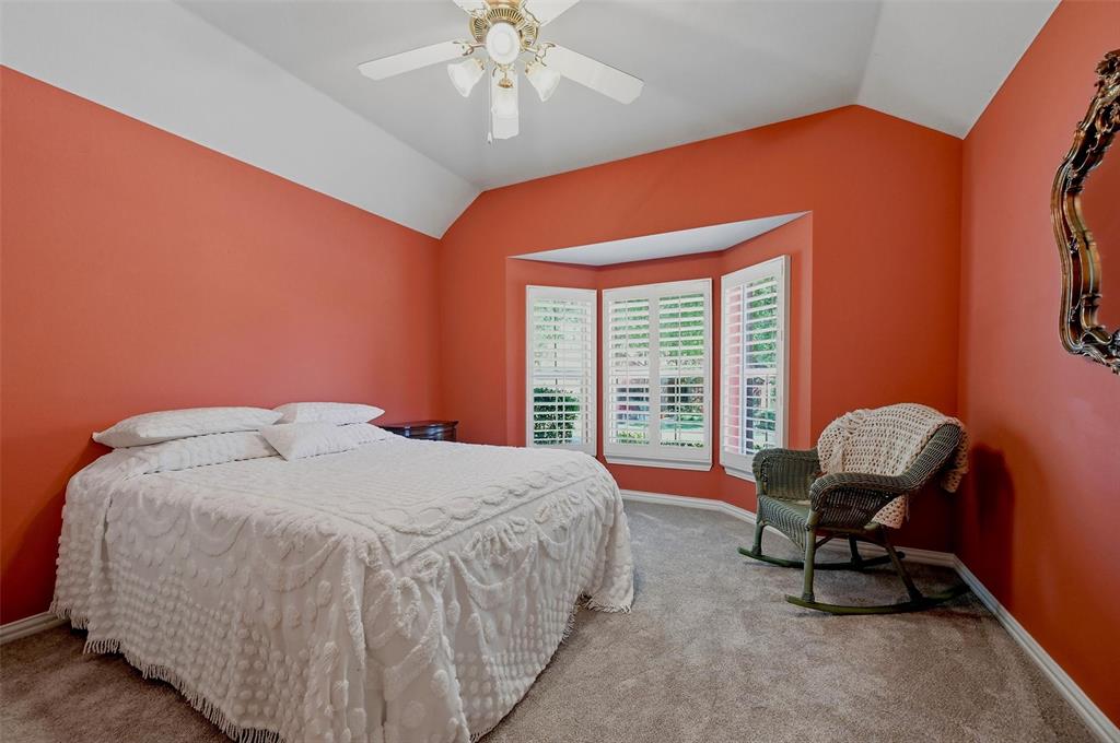 Vaulted ceiling featuring a central lighted ceiling fan, bay window with plantation shutters, and neutral carpeting