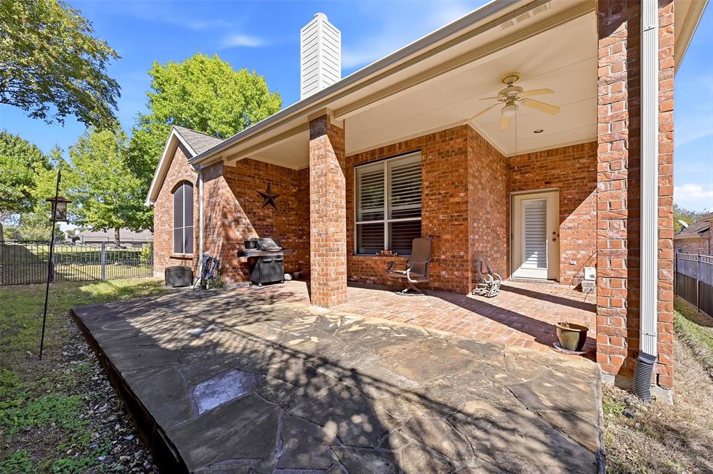 Covered brick patio featuring stone pavers, a ceiling fan, and a exterior brick chimney