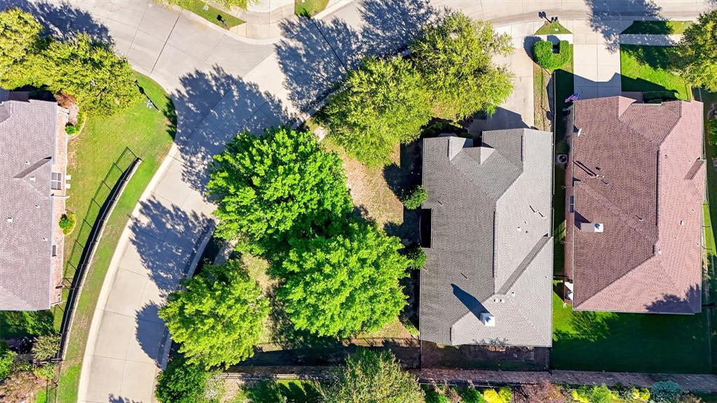 Aerial perspective of a corner lot featuring mature trees, a multi-pitched roofline, an exterior chimney, and a private rear yard with perimeter fencing