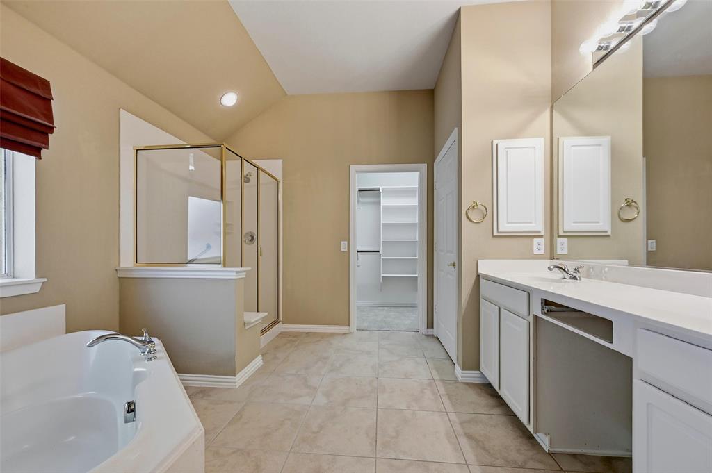 Bathroom featuring a soaking tub, glass-enclosed shower with gold-tone hardware, white dual-sink vanity with light-toned countertop, and built-in closet shelving