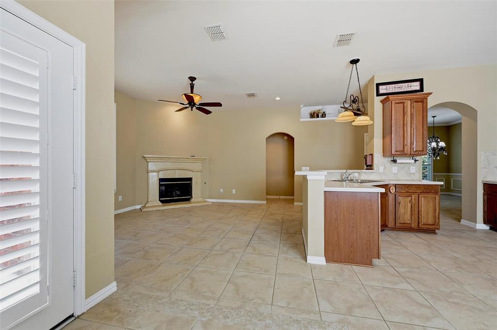 Open-concept interior featuring tile flooring, a fireplace with a decorative mantel, wood cabinetry, stone-style countertops, and arched entryways