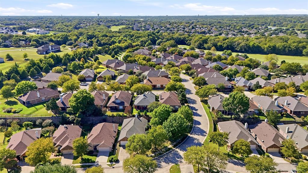 Aerial perspective of a residential neighborhood featuring paved streets, mature trees, dense greenery, and detached homes with shingled rooflines
