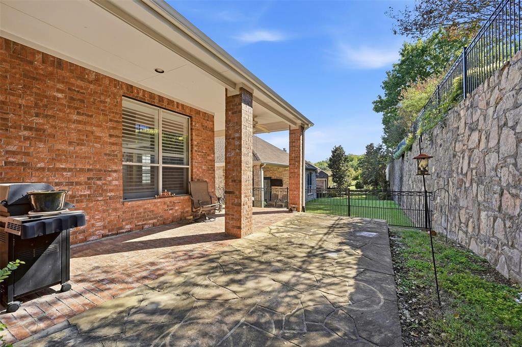 Covered patio with brick exterior and stone paver flooring, featuring a large tiered stone retaining wall and metal perimeter fencing