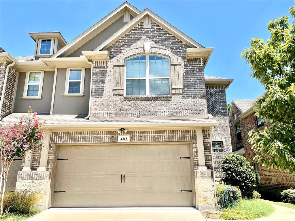 Multi-level brick and stone façade featuring decorative shutters, a gabled roofline, an arched window, and an attached two-car garage Multi-level brick and stone façade featuring decorative shutters, a gabled roofline, an arched window, and an attached two-car garage