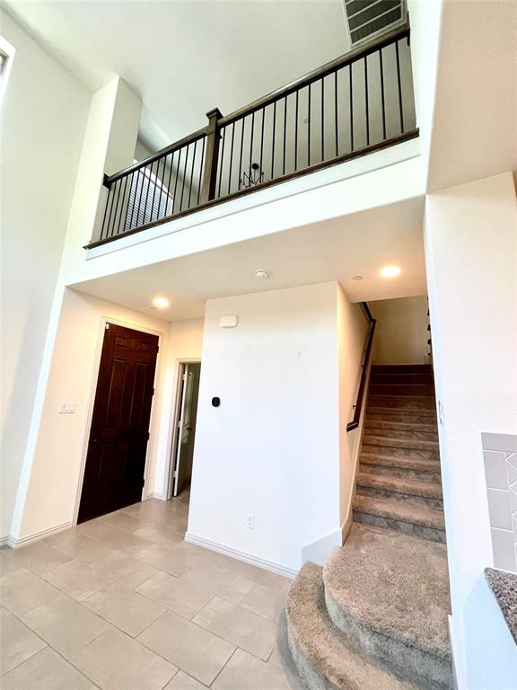 High-ceiling entryway featuring ceramic tile flooring, a staircase with carpeted treads, and a landing with a dark-finished metal balustrade
