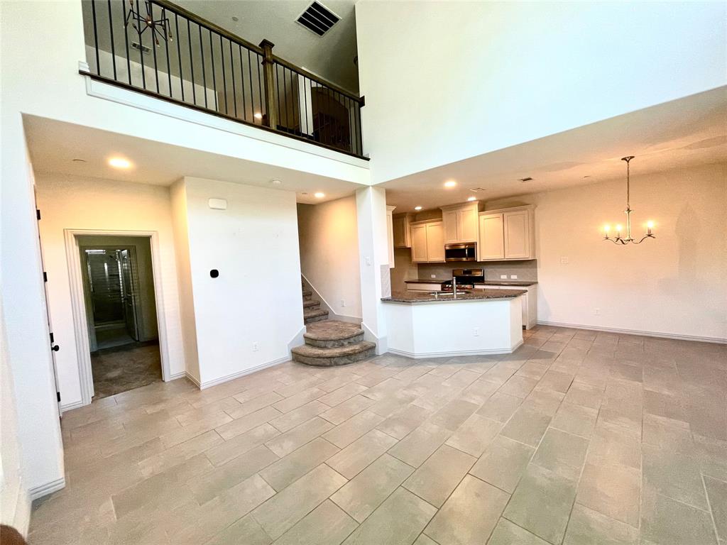 Open-concept interior featuring double-height ceilings, a multi-level staircase with carpeted treads, a kitchen island with stone-finish countertops, light-toned cabinetry, and tile flooring