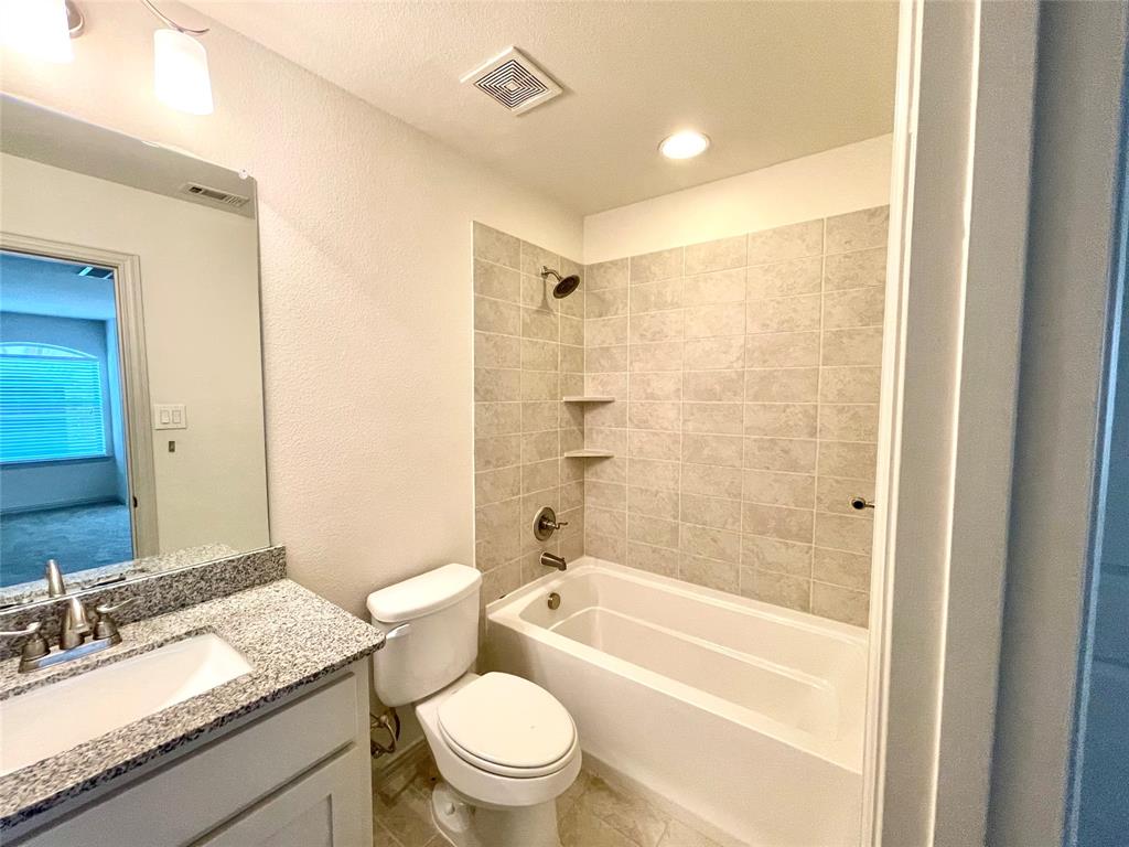 Full bathroom featuring a stone-composite countertop with an integrated sink, large wall-mounted mirror, white cabinetry, and a shower-tub combination with tiled surround walls and built-in shelving