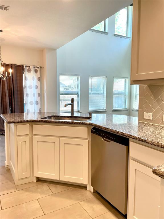 Kitchen featuring a stone countertop, stainless steel dishwasher, shaker-style cabinetry, herringbone-patterned tile backsplash, and double-height ceiling with clerestory windows