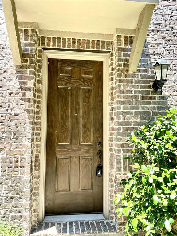 Entryway featuring a wood-finish door, brick exterior facade, metal lantern-style light fixture, and arched covered threshold