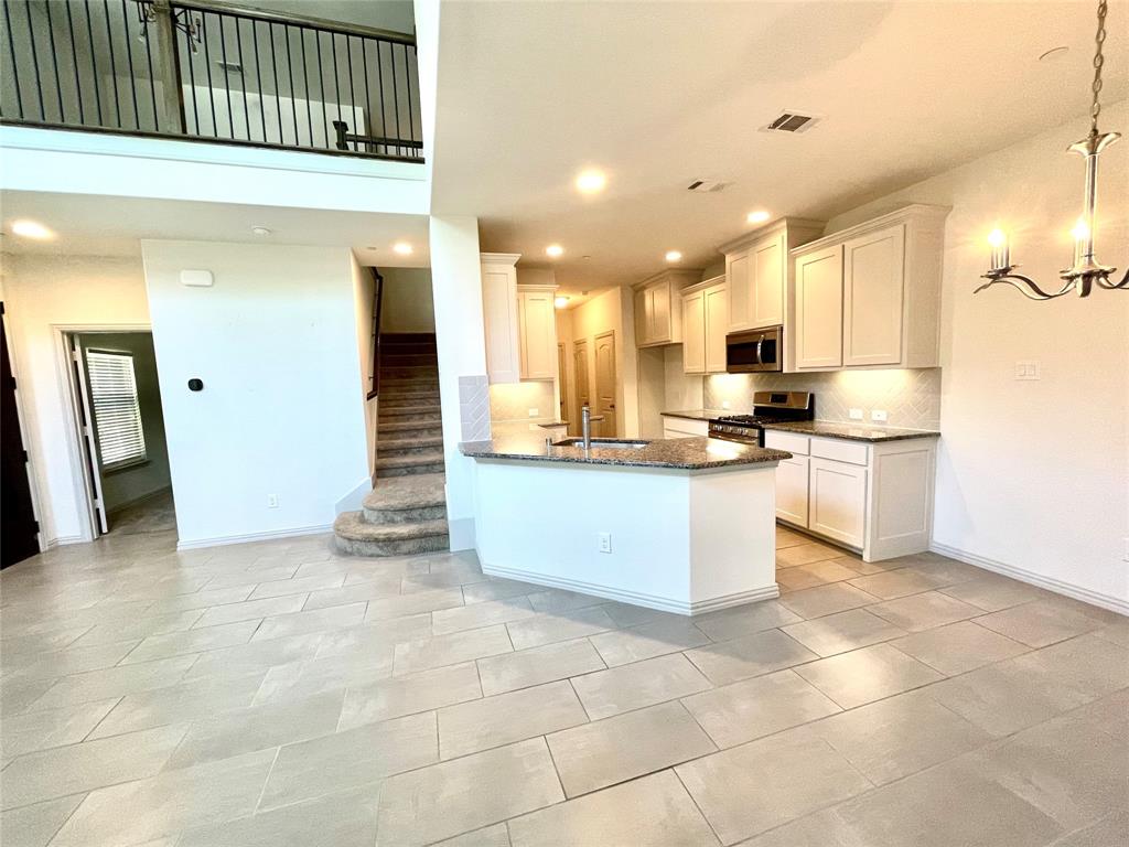 Kitchen featuring light-toned cabinetry, stone-finish countertops, and stainless steel built-in appliances, complemented by tile flooring, a two-story ceiling, and a metal balustrade