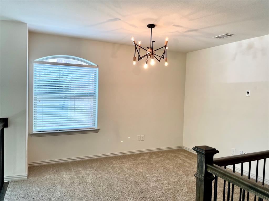 Multi-arm sputnik-style chandelier, arched-top window with horizontal blinds, neutral wall-to-wall carpeting, and wood-finish banister with metal spindles