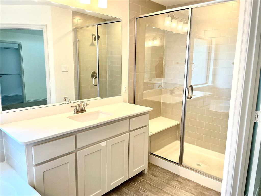 Bathroom featuring a white cabinetry vanity with a solid surface countertop, rectangular under-mount sink, walk-in shower with a glass enclosure and built-in bench, subway tile shower surround, and wood-finish flooring