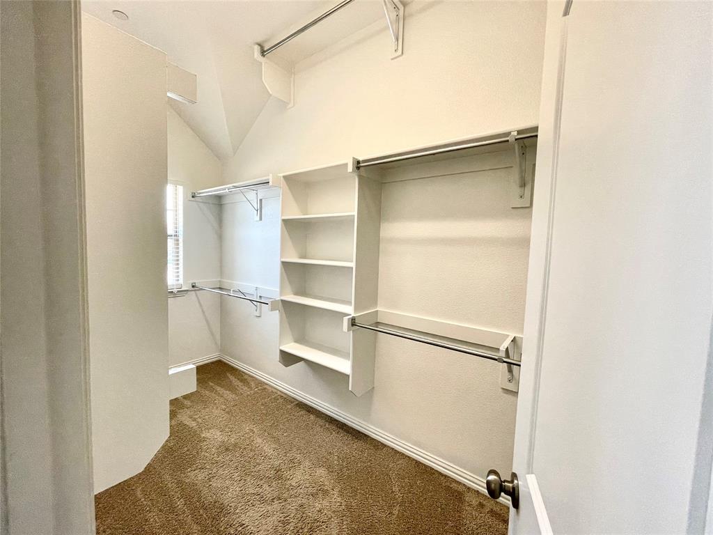 Walk-in closet featuring vaulted ceilings, built-in shelving, multiple hanging rods, and carpeting