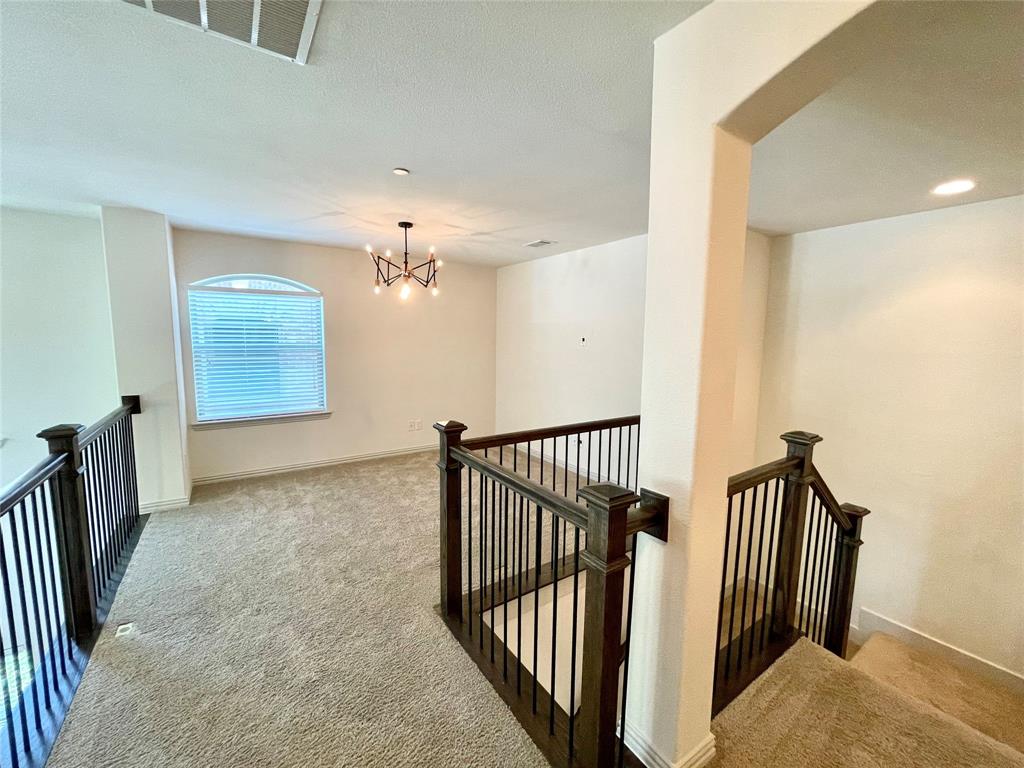 Open interior space featuring arched window, wall-to-wall carpeting, multi-arm chandelier, and staircase with wooden handrails and metal balusters