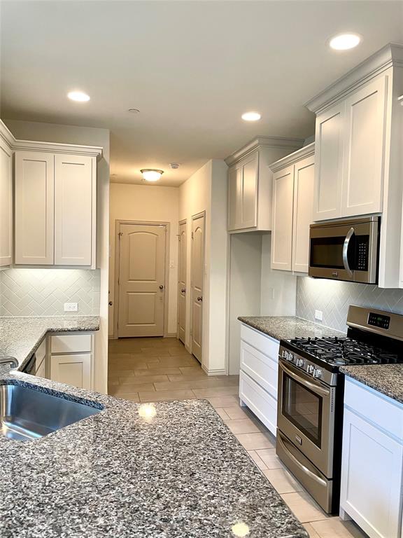 Kitchen featuring white shaker-style cabinetry, stone countertops, stainless steel appliances, a herringbone-patterned tile backsplash, and recessed lighting
