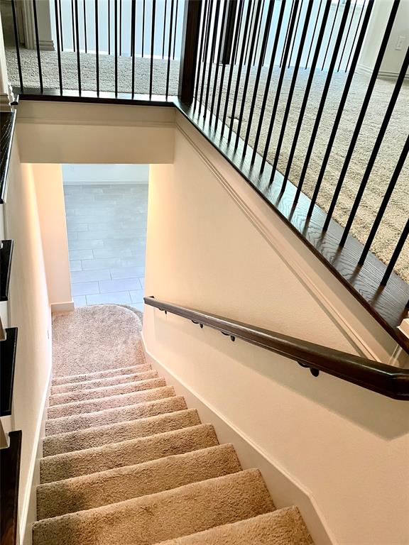 Staircase featuring wall-to-wall carpeting, wood-finish handrail, and a black metal balustrade