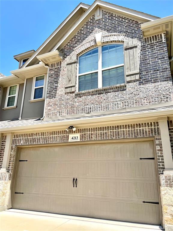 Multi-story exterior featuring multi-toned brick masonry, arched window detailing with decorative wood-finish shutters, and a two-car panel garage door with decorative iron-style hardware