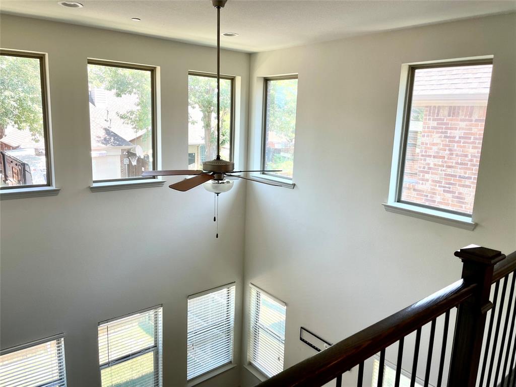 Double-height ceiling featuring large windows, recessed lighting, a central ceiling fan with integrated light fixture, and a wooden handrail