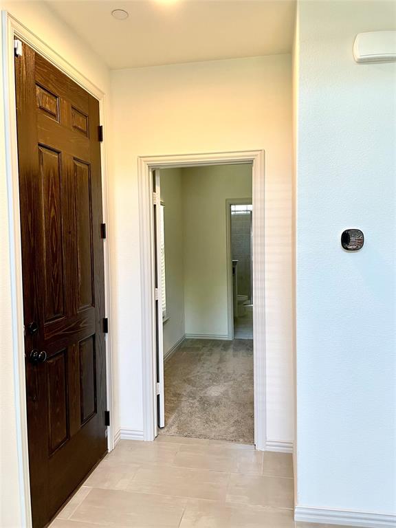 Stained wood six-panel door with matte black hardware, neutral tile flooring, and integrated wall-mounted thermostat