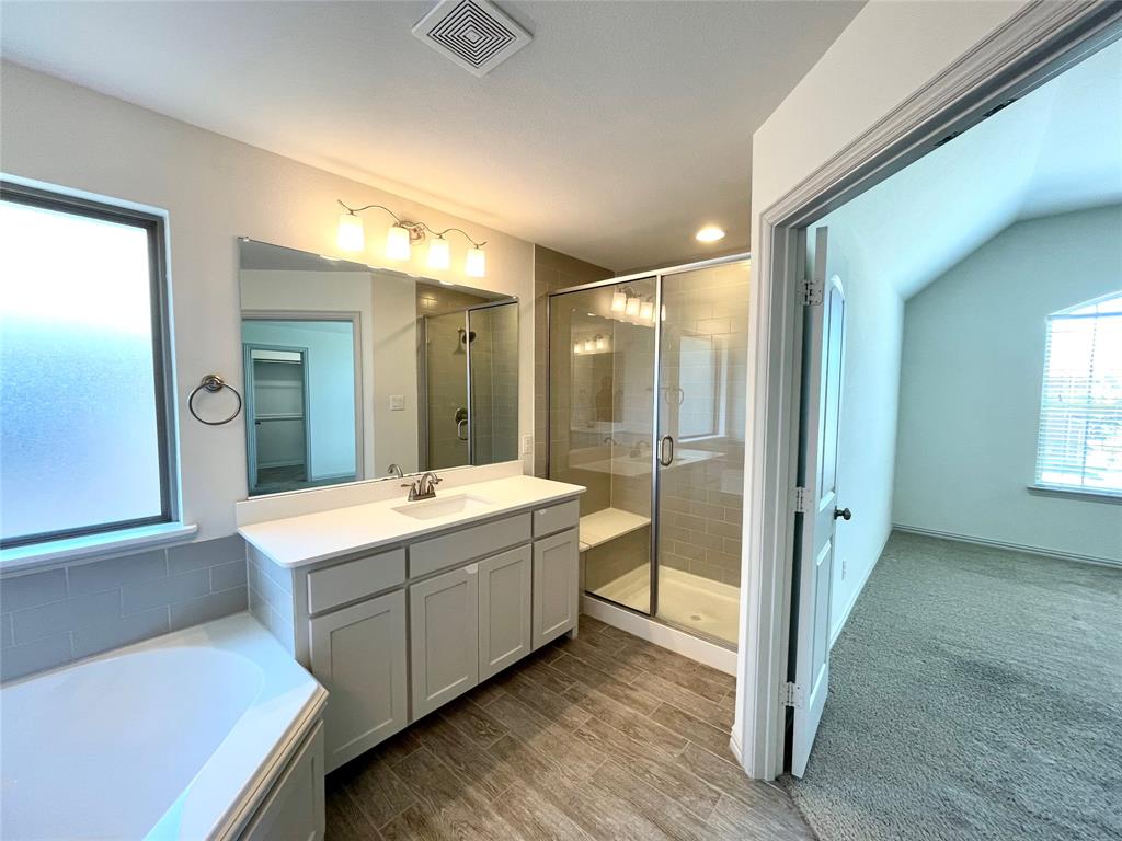 Bathroom featuring a vanity with white countertop, shower enclosure with tiled surround and built-in bench, deep soaking tub, and wood-finish flooring
