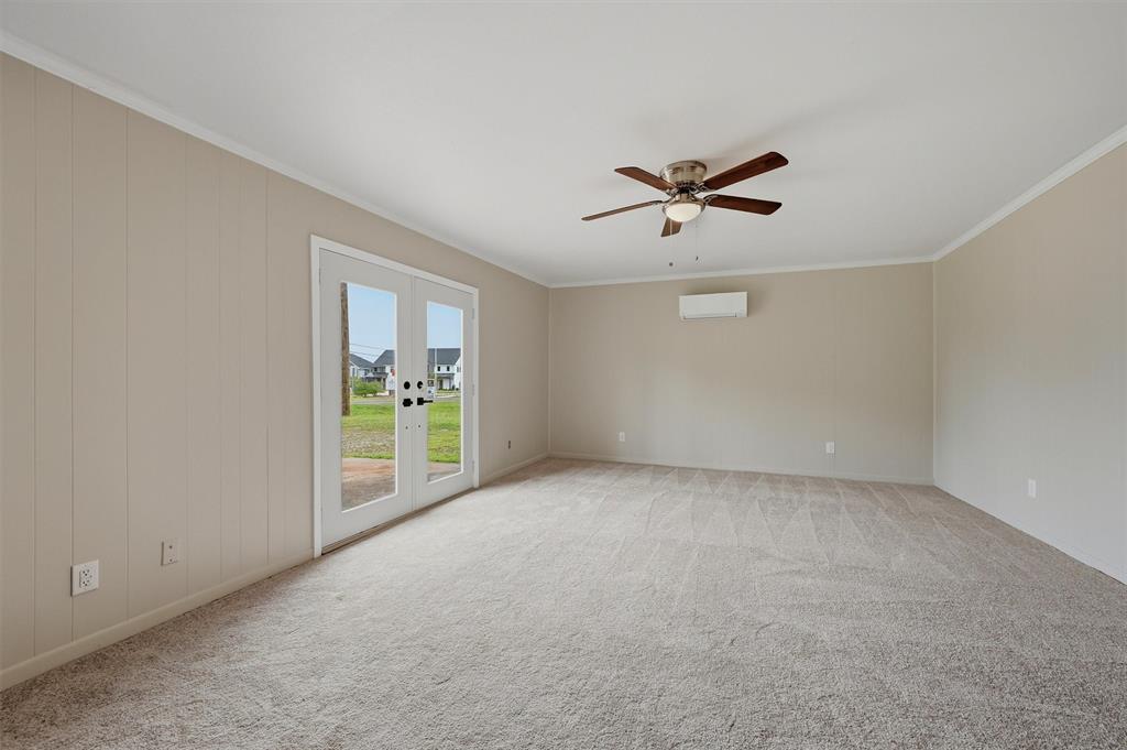 Neutral-toned interior featuring wall-to-wall carpeting, vertical paneling, a multi-speed ceiling fan with integrated lighting, and a wall-mounted ductless heating and cooling unit, complete with a glass-paneled exterior door Neutral-toned interior featuring wall-to-wall carpeting, vertical paneling, a multi-speed ceiling fan with integrated lighting, and a wall-mounted ductless heating and cooling unit, complete with a glass-paneled exterior door
