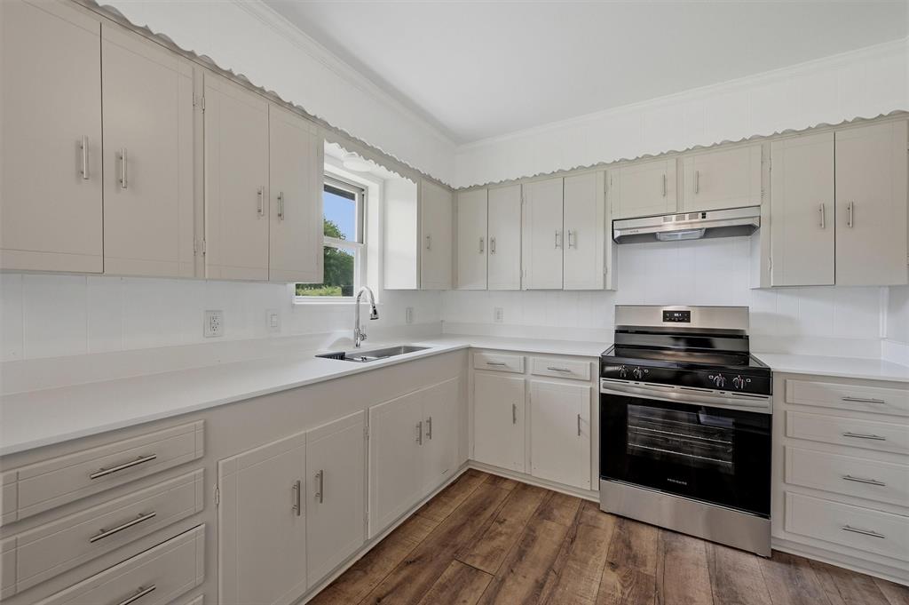 Kitchen featuring neutral-toned cabinetry, white countertops, stainless steel range with overhead vent hood, under-mount sink, and wood-finish flooring
