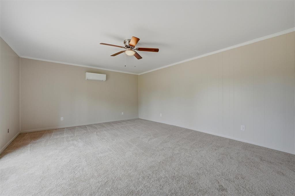 Neutral wall paneling, wall-mounted ductless heating and cooling unit, ceiling fan with light kit, and neutral carpeting Neutral wall paneling, wall-mounted ductless heating and cooling unit, ceiling fan with light kit, and neutral carpeting