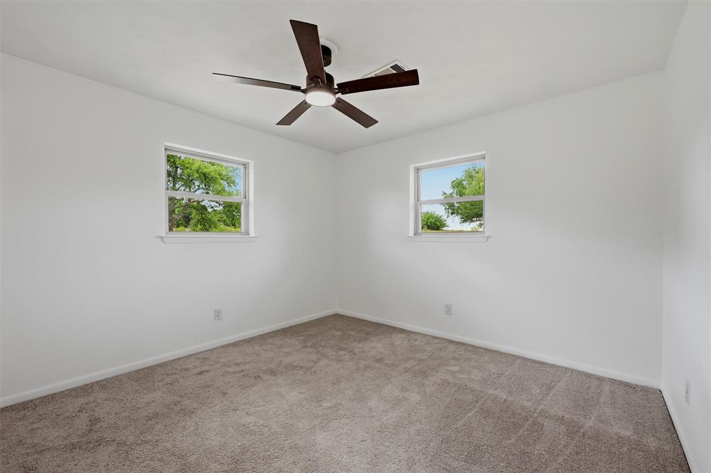 Neutral interior featuring plush wall-to-wall carpeting, two dual-pane windows, and a central ceiling fan with integrated light fixture