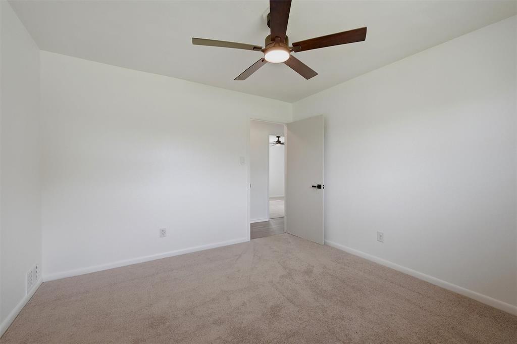 Neutral-toned carpeting, matte white walls, and a ceiling fan with integrated lighting