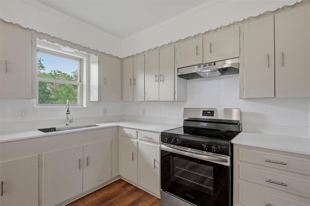 Kitchen featuring solid-surface countertops, wood-finish flooring, shaker-style cabinetry with satin nickel pulls, a stainless steel range, and a drop-in sink with a high-arc faucet