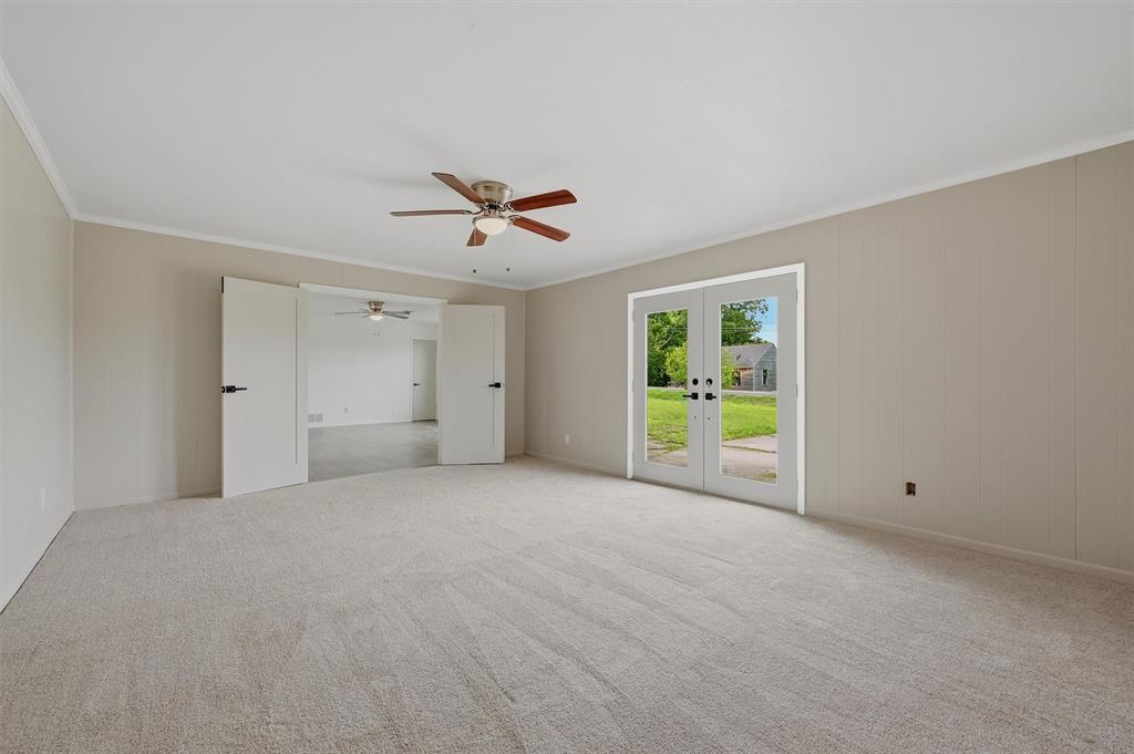Neutral-toned interior space featuring wall-to-wall carpeting, a ceiling fan with integrated lighting, dual-panel interior doors, and a double glass door exterior entrance Neutral-toned interior space featuring wall-to-wall carpeting, a ceiling fan with integrated lighting, dual-panel interior doors, and a double glass door exterior entrance