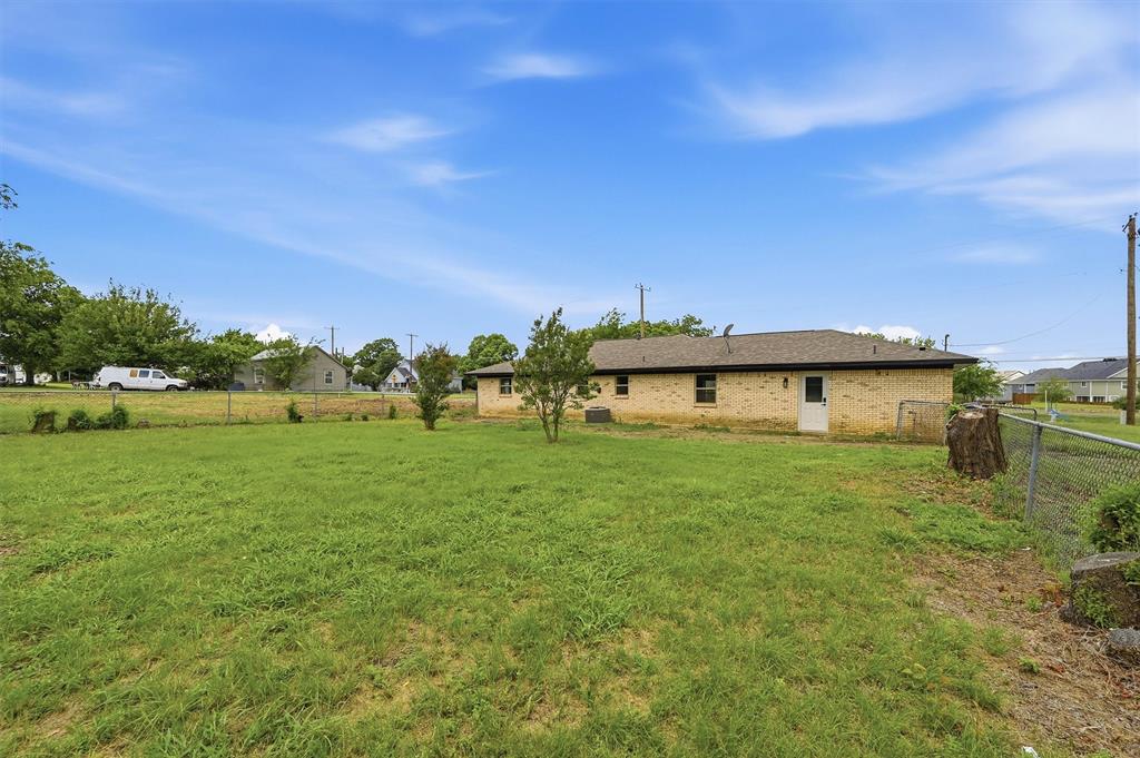 Expansive backyard featuring a grass lawn, chain-link fencing, masonry exterior walls, and a shingle roof