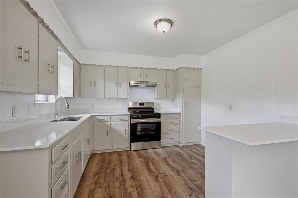Kitchen featuring light-toned cabinetry, quartz countertops, stainless steel gas range, wood-finish flooring, and a flush-mount ceiling light fixture