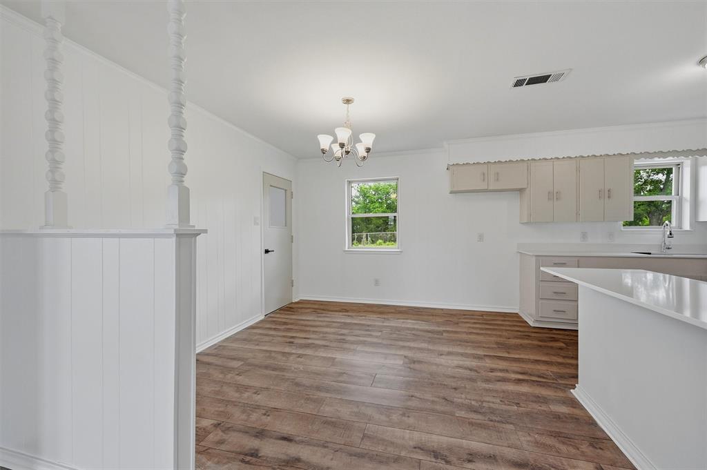 Interior space featuring wood-finish flooring, a multi-arm chandelier, decorative spindle room divider, and cabinetry with stone countertops