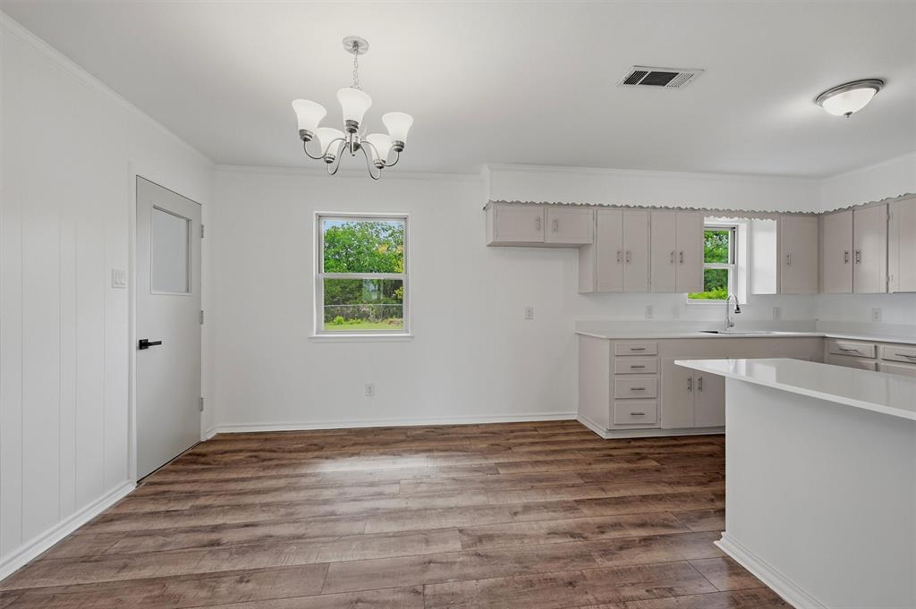 Kitchen featuring light-toned cabinetry, solid surface countertops, wood-finish flooring, a multi-arm chandelier, and a neutral color palette