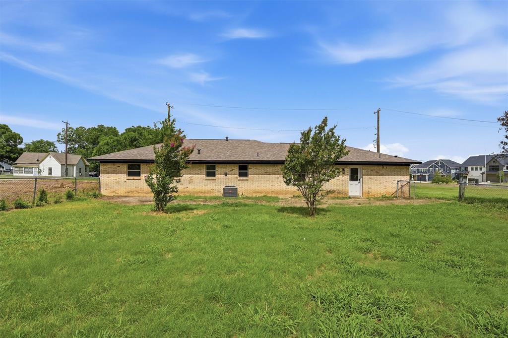 Single-story residence featuring a brick exterior, hipped roof, grass-covered backyard, and mature trees