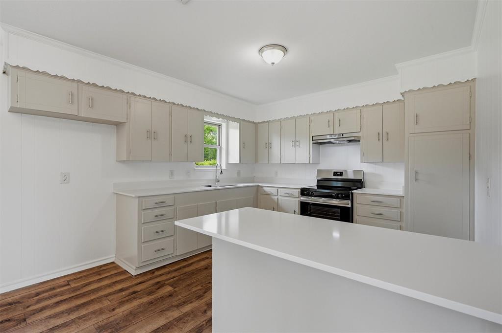 Kitchen featuring light-toned cabinetry, solid-surface countertops, wood-finish flooring, a stainless steel range, and a breakfast bar